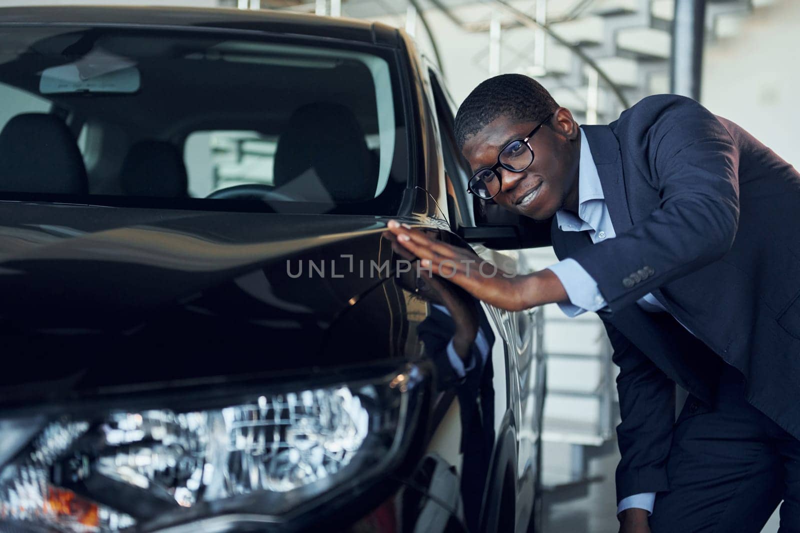 Young african american businessman in black suit is the autosalon.