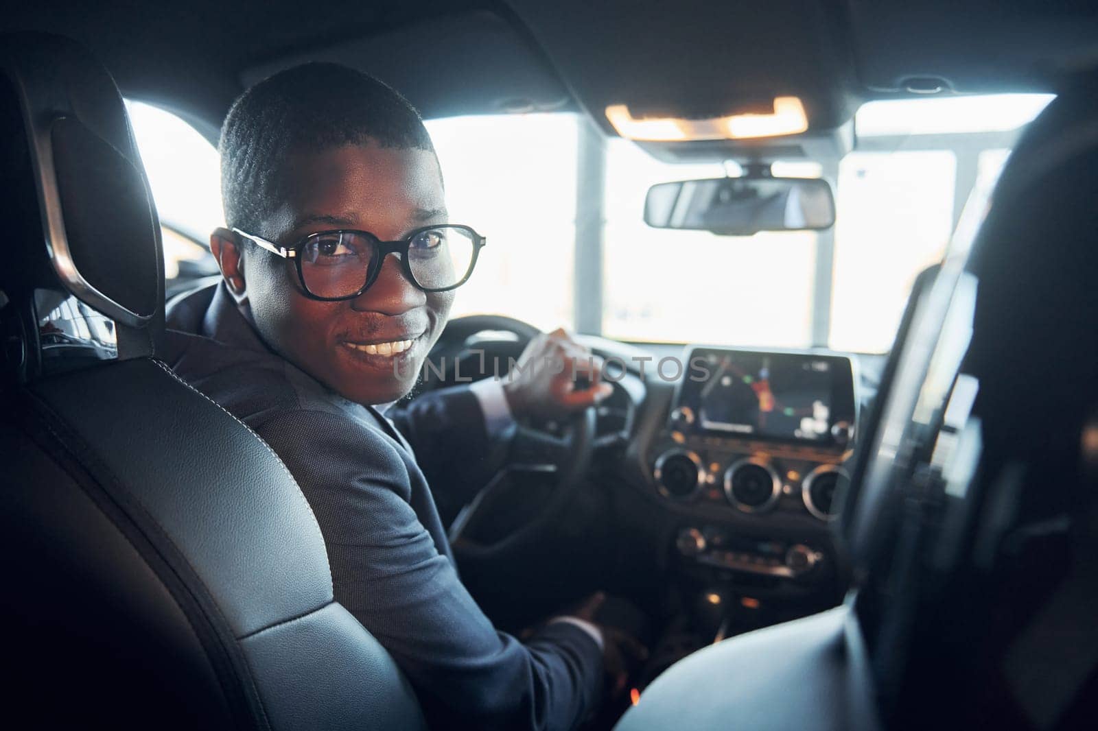 Vehicle interior. Young african american businessman in black suit is in the automobile.