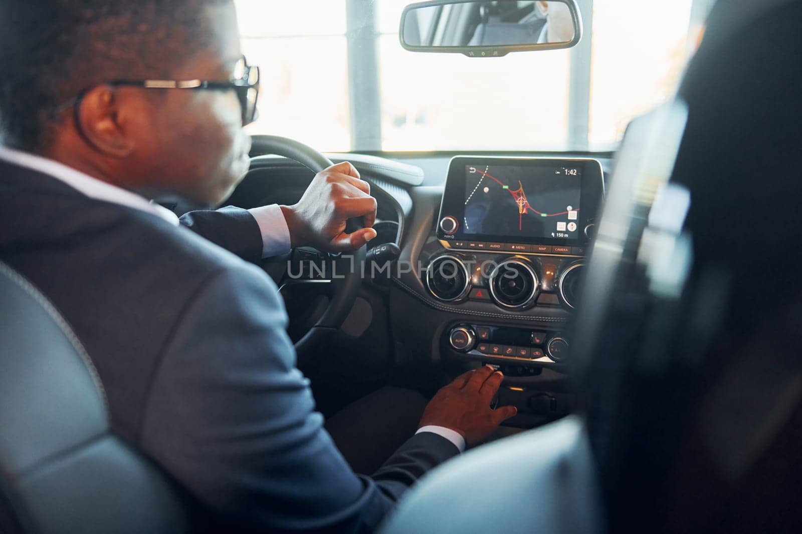 Rear view. Young african american businessman in black suit is in the automobile.