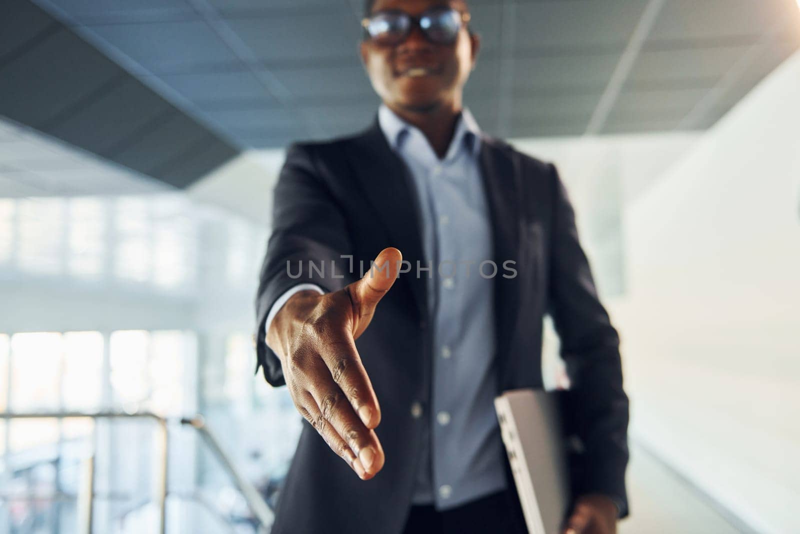 Handshake gesture. Young african american businessman in black suit is indoors.