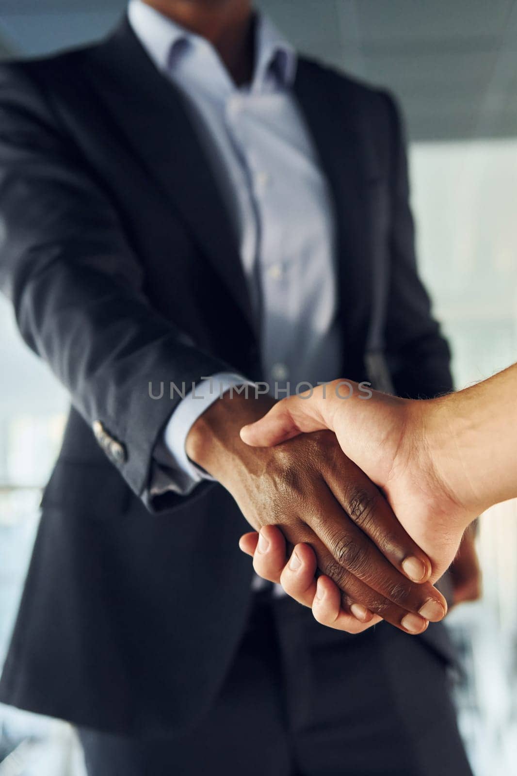 Doing handshake with customer. Young african american businessman in black suit is indoors.