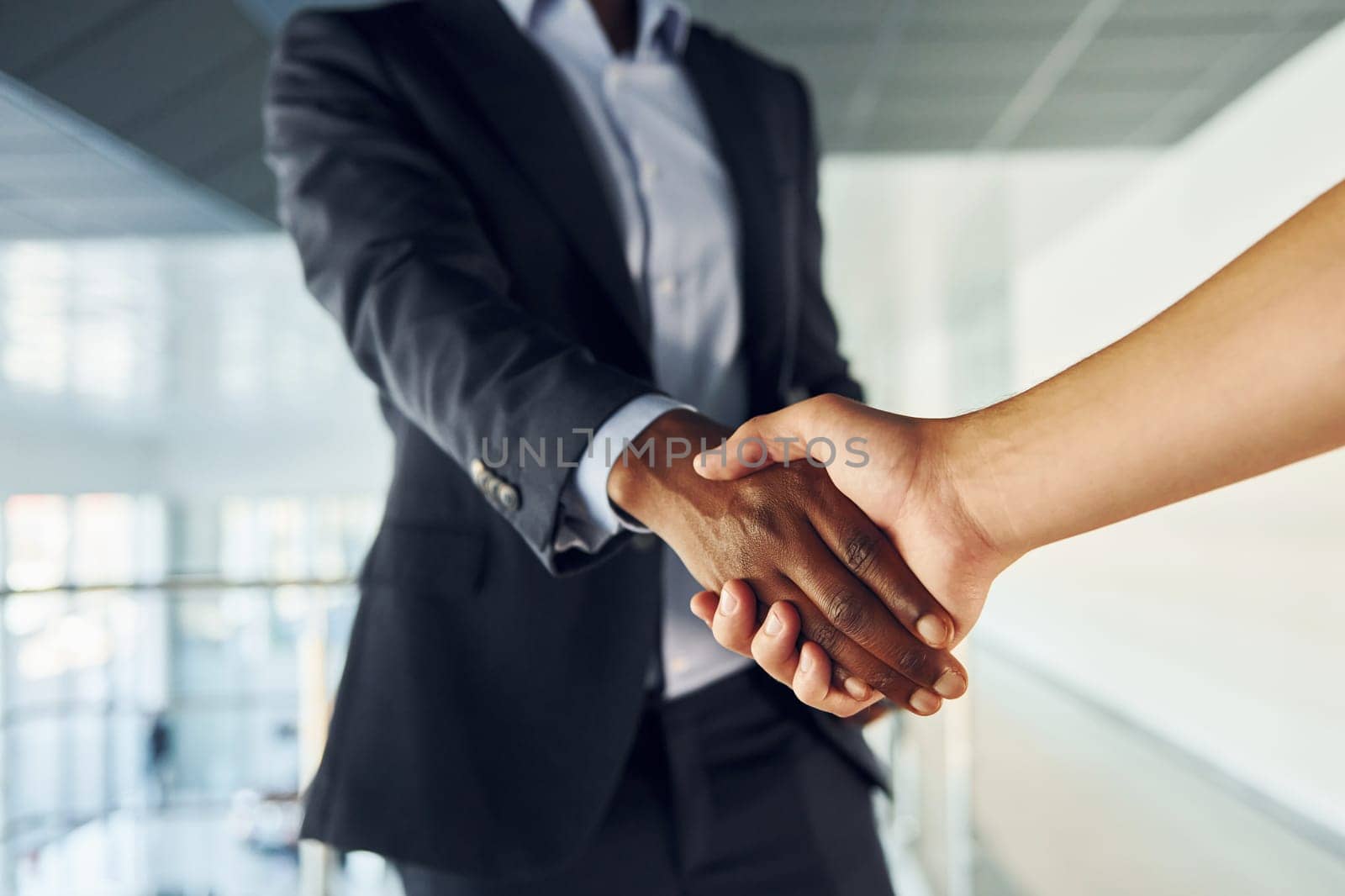 Doing handshake with customer. Young african american businessman in black suit is indoors.