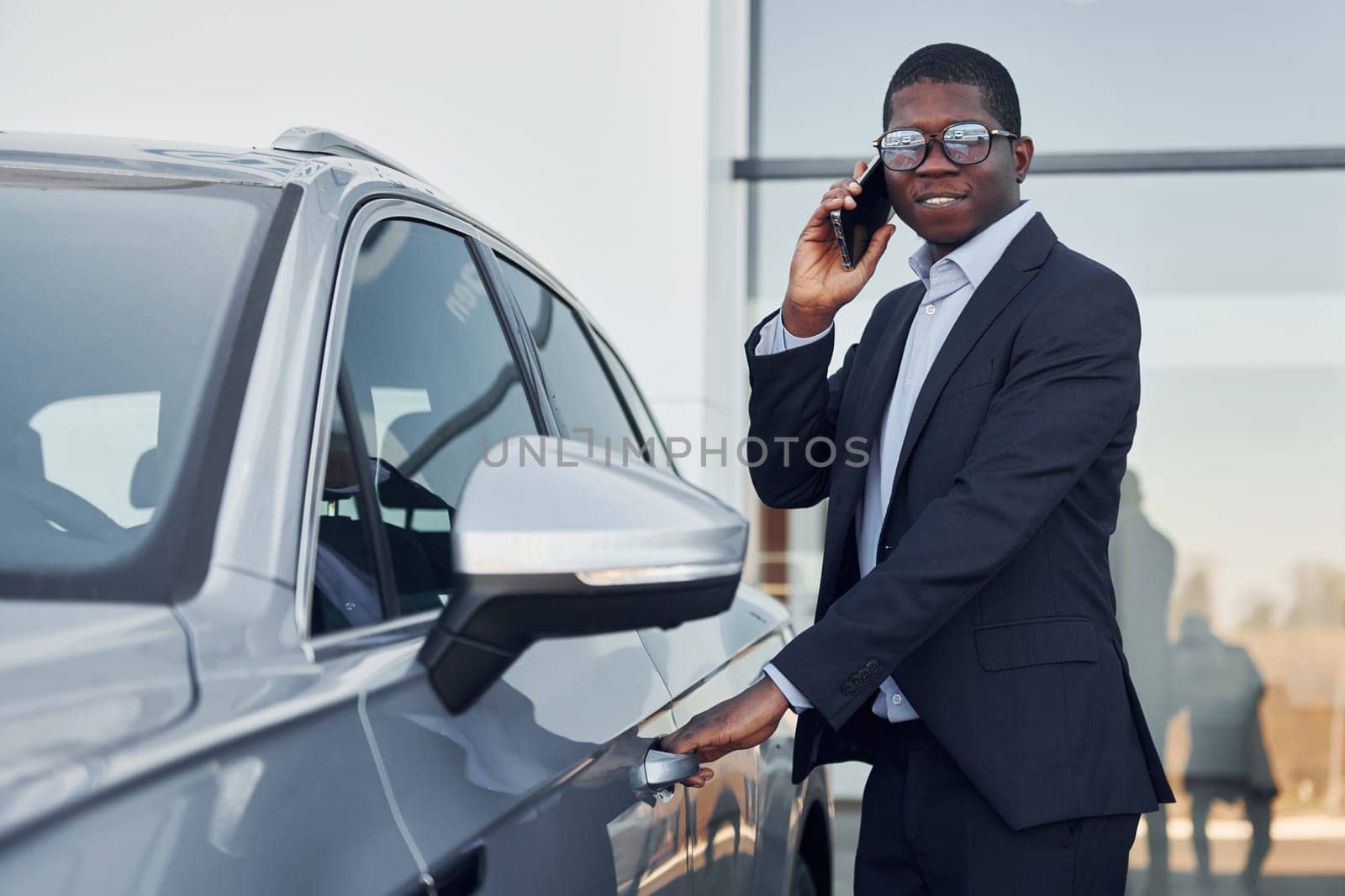 Young african american businessman in black suit is near automobile outdoors.