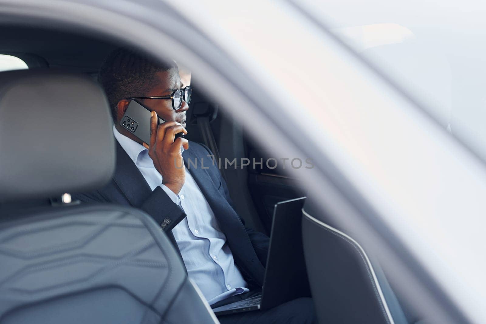 Passanger on the back seat. Young african american businessman in black suit is in the automobile.