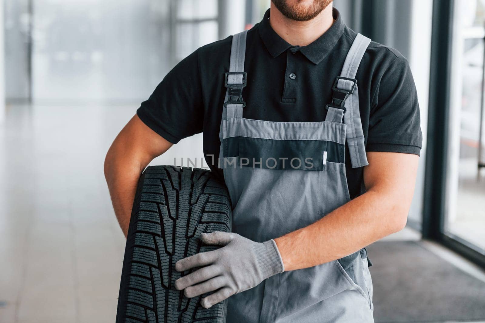 Holding tire. Man in uniform is working in the autosalon at daytime.