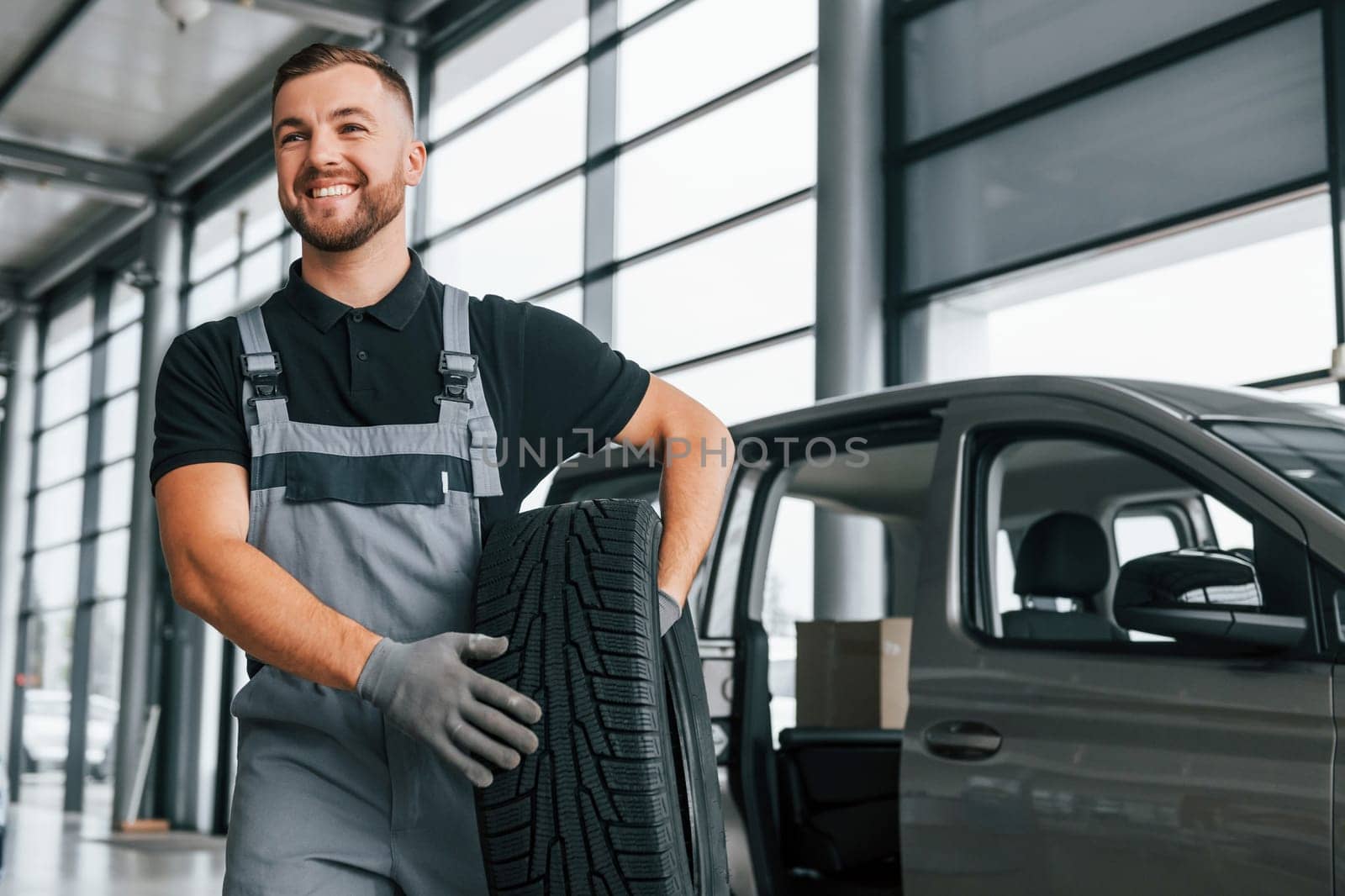 Brand new tire. Man in uniform is working in the autosalon at daytime.