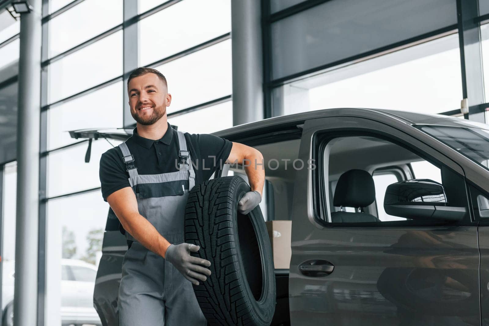 Brand new tire. Man in uniform is working in the autosalon at daytime.