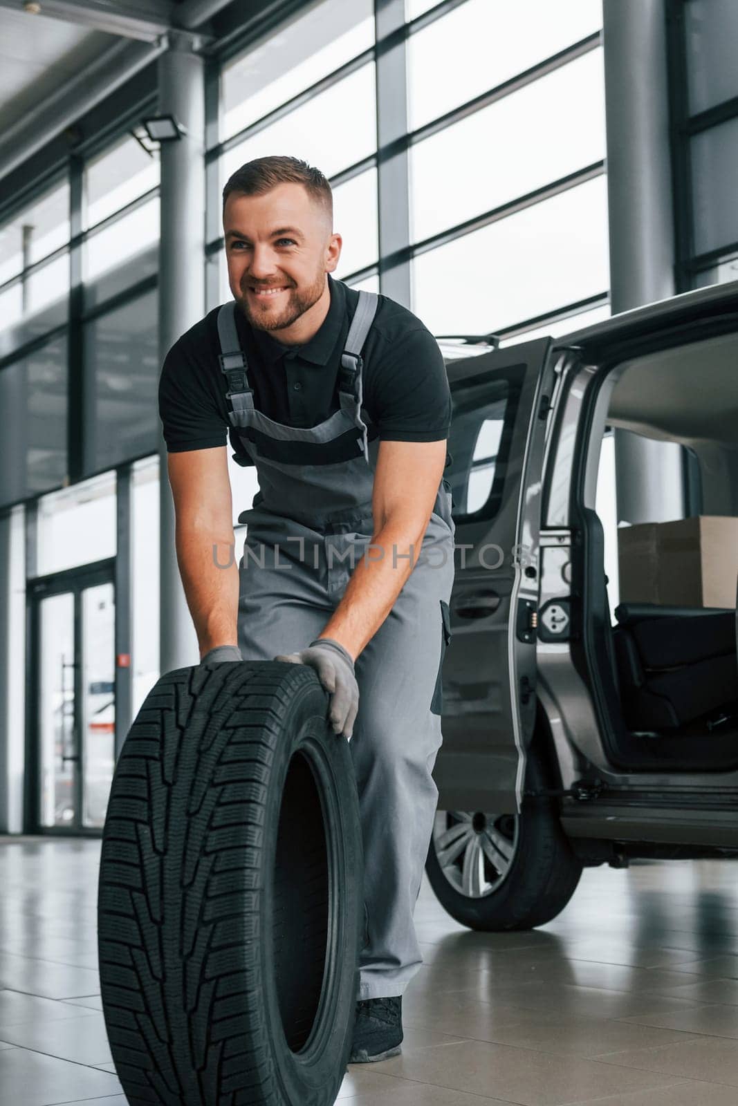 Brand new tire. Man in uniform is working in the autosalon at daytime.