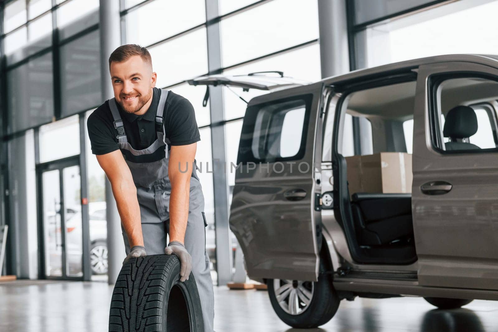 Time to change tires. Man in uniform is working in the autosalon at daytime.