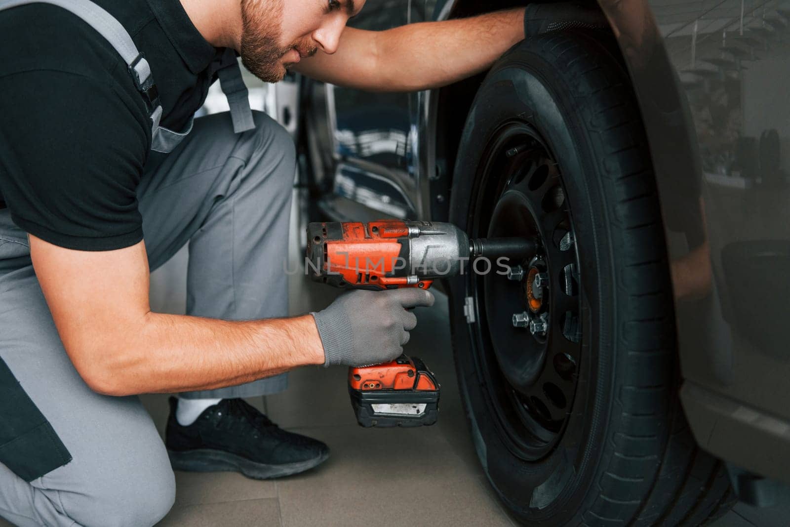 Changing of the tires. Man in uniform is working in the autosalon at daytime.