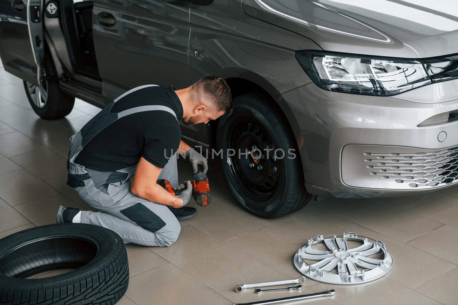 Changing of the tires. Man in uniform is working in the autosalon at daytime.