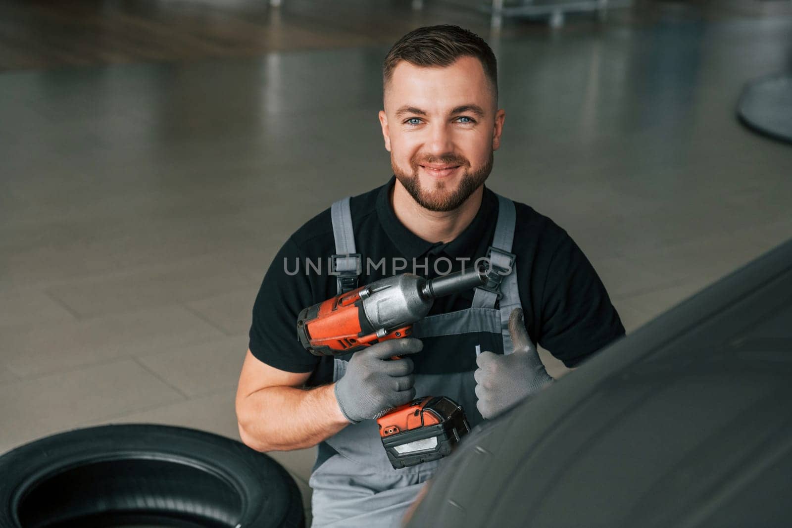 Using equipment. Man in uniform is working in the autosalon at daytime.