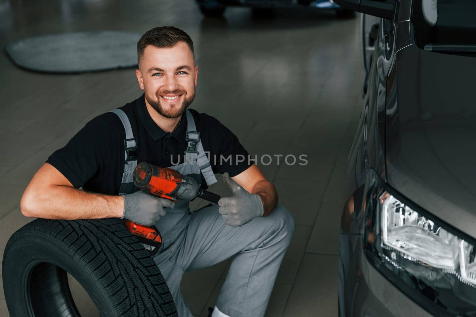 Using equipment. Man in uniform is working in the autosalon at daytime.