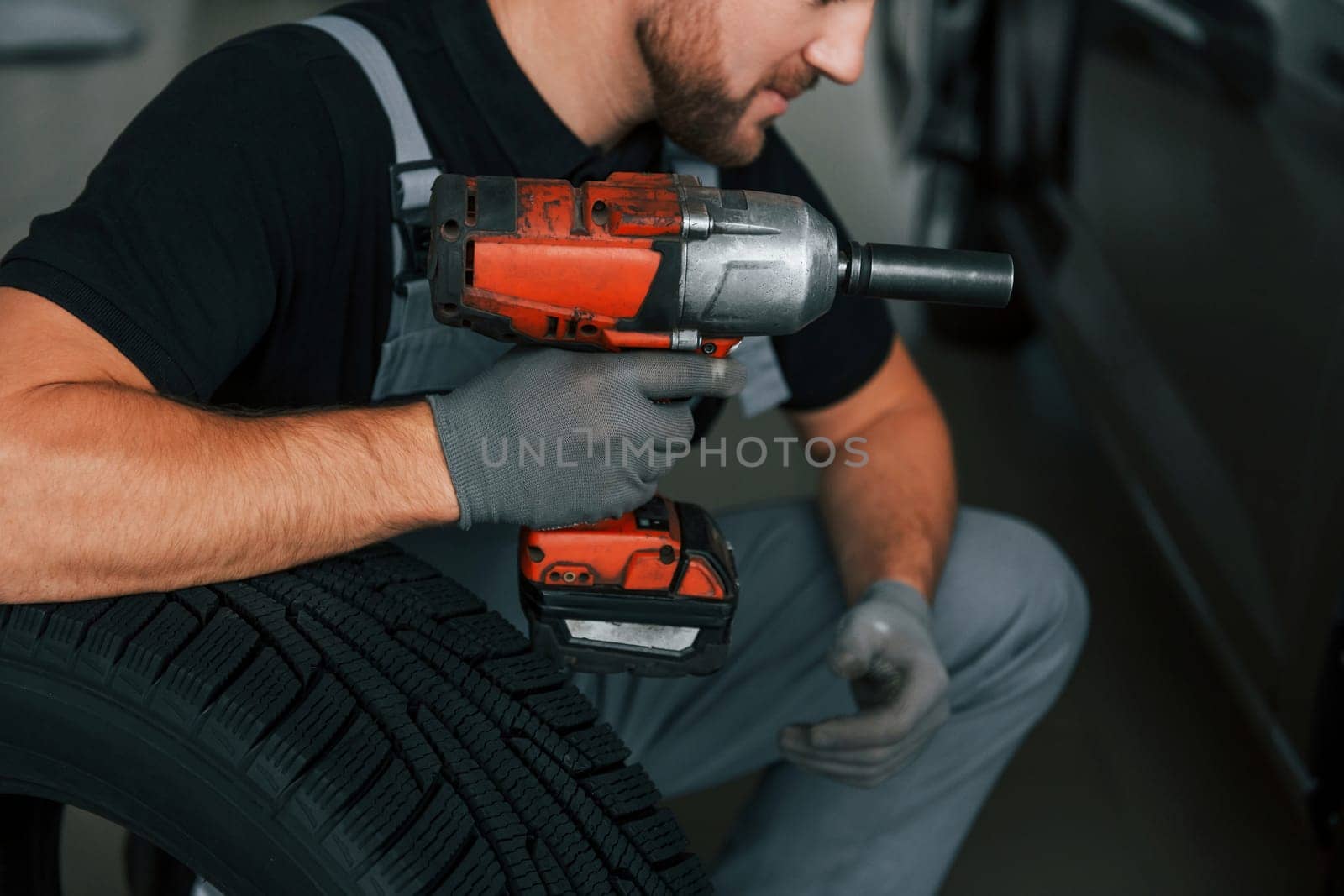 Using equipment. Man in uniform is working in the autosalon at daytime.