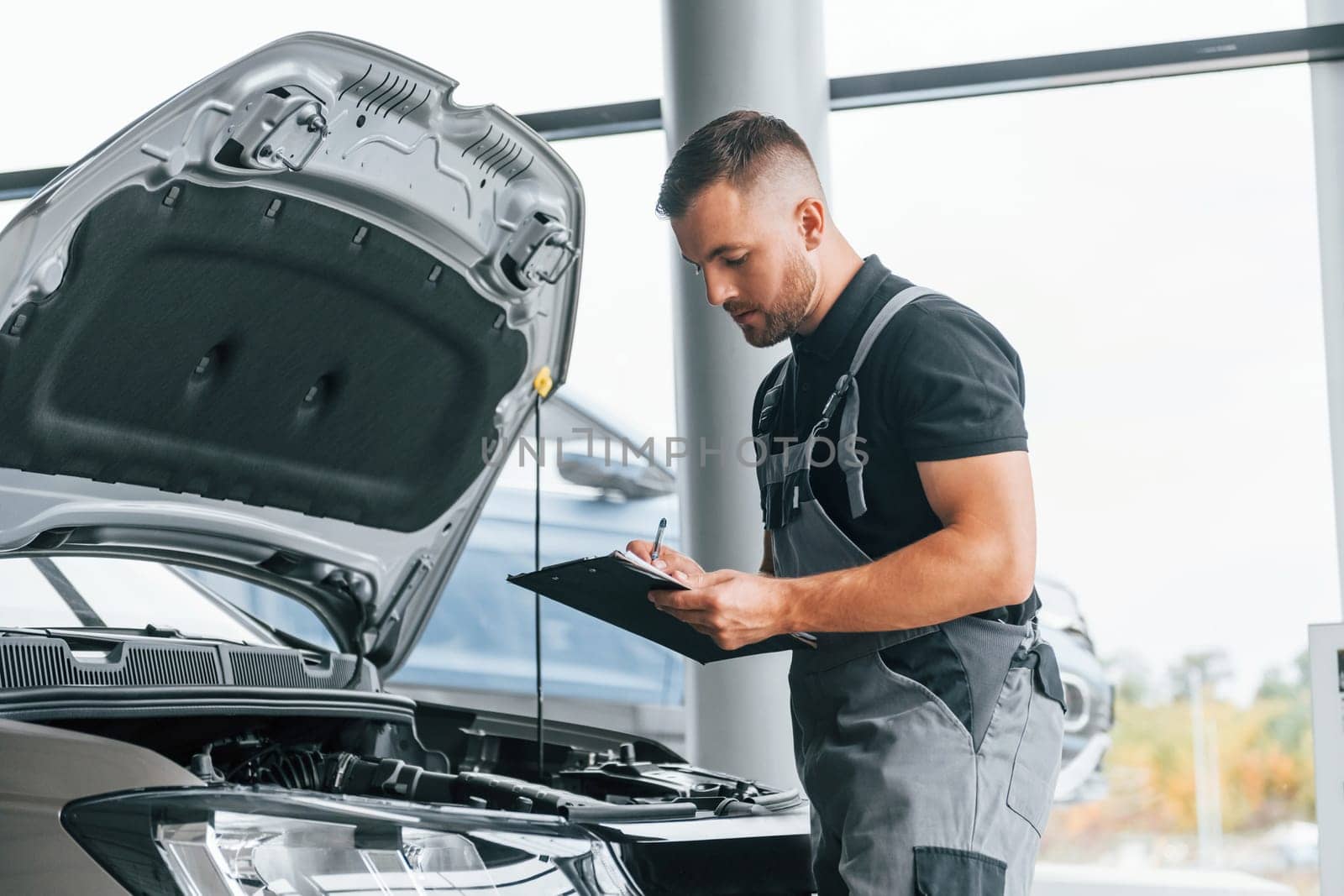 Repairing of the car. Man in uniform is working in the autosalon at daytime.