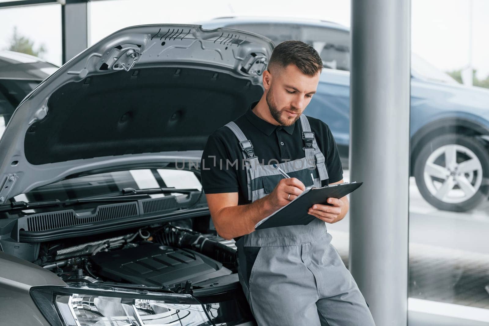 With notepad. Man in uniform is working in the autosalon at daytime.