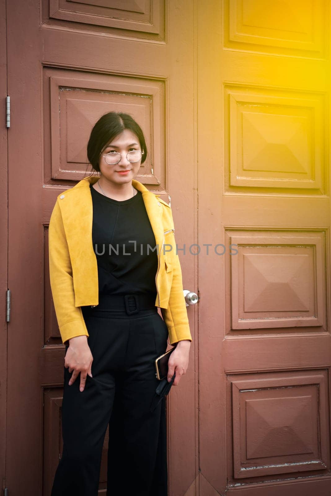 Beautiful asian woman (LGBTQ) natural makeup wear fashion yellow leather clothes with glasses posing at old town and vintage building outdoor fashion style