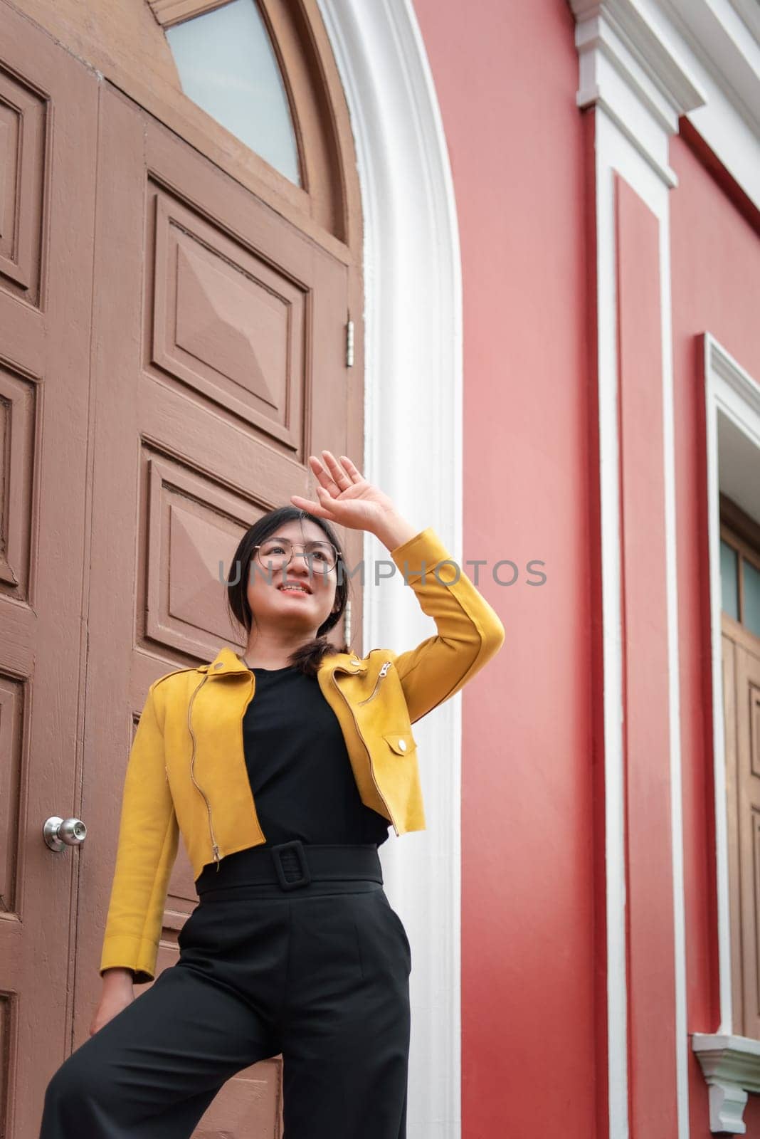 Beautiful asian woman (LGBTQ) natural makeup wear fashion yellow leather clothes with glasses posing at old town and vintage building outdoor fashion style