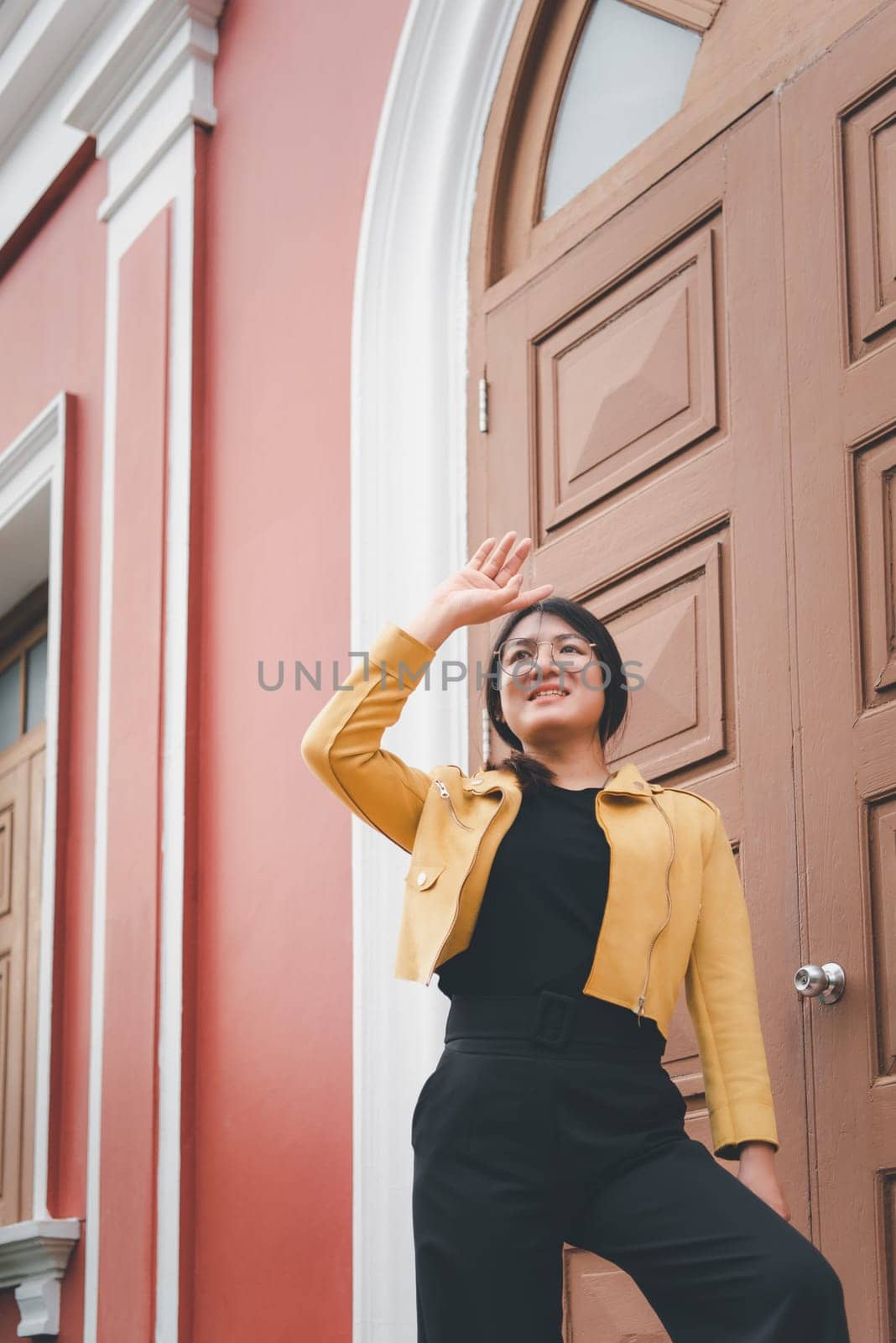 Beautiful asian woman (LGBTQ) natural makeup wear fashion yellow leather clothes with glasses posing at old town and vintage building outdoor fashion style