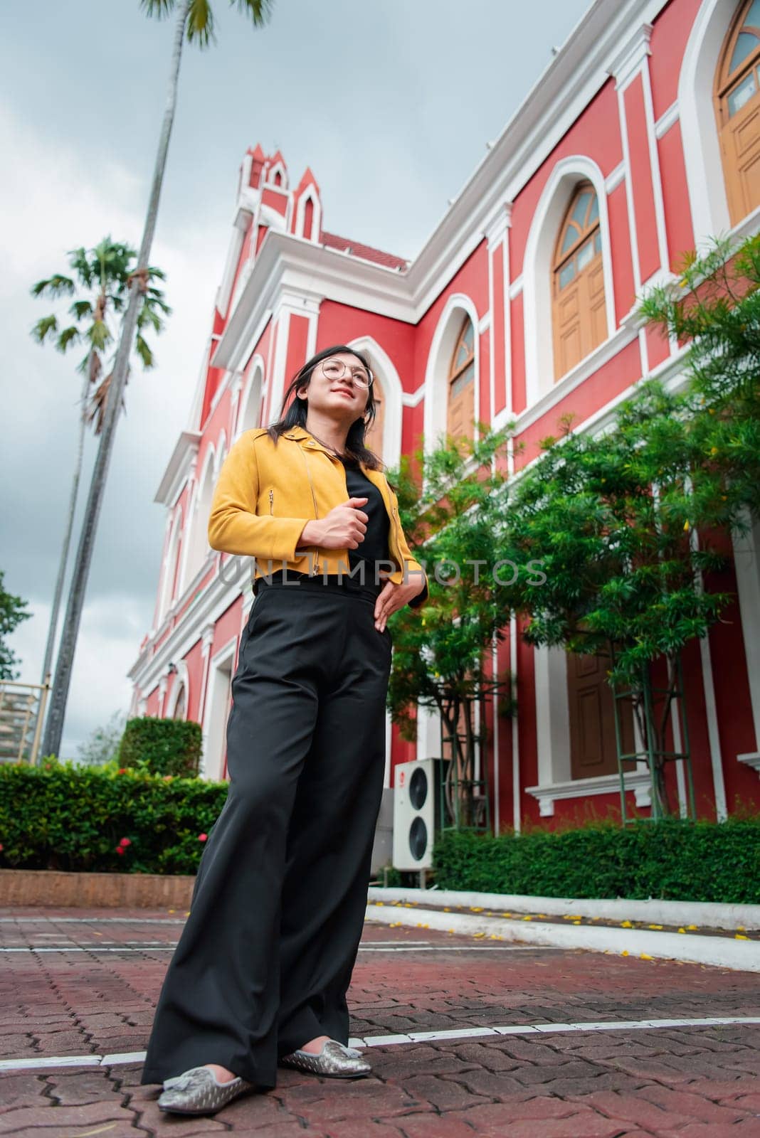 Beautiful asian woman (LGBTQ) natural makeup wear fashion yellow leather clothes with glasses posing at old town and vintage building outdoor fashion style