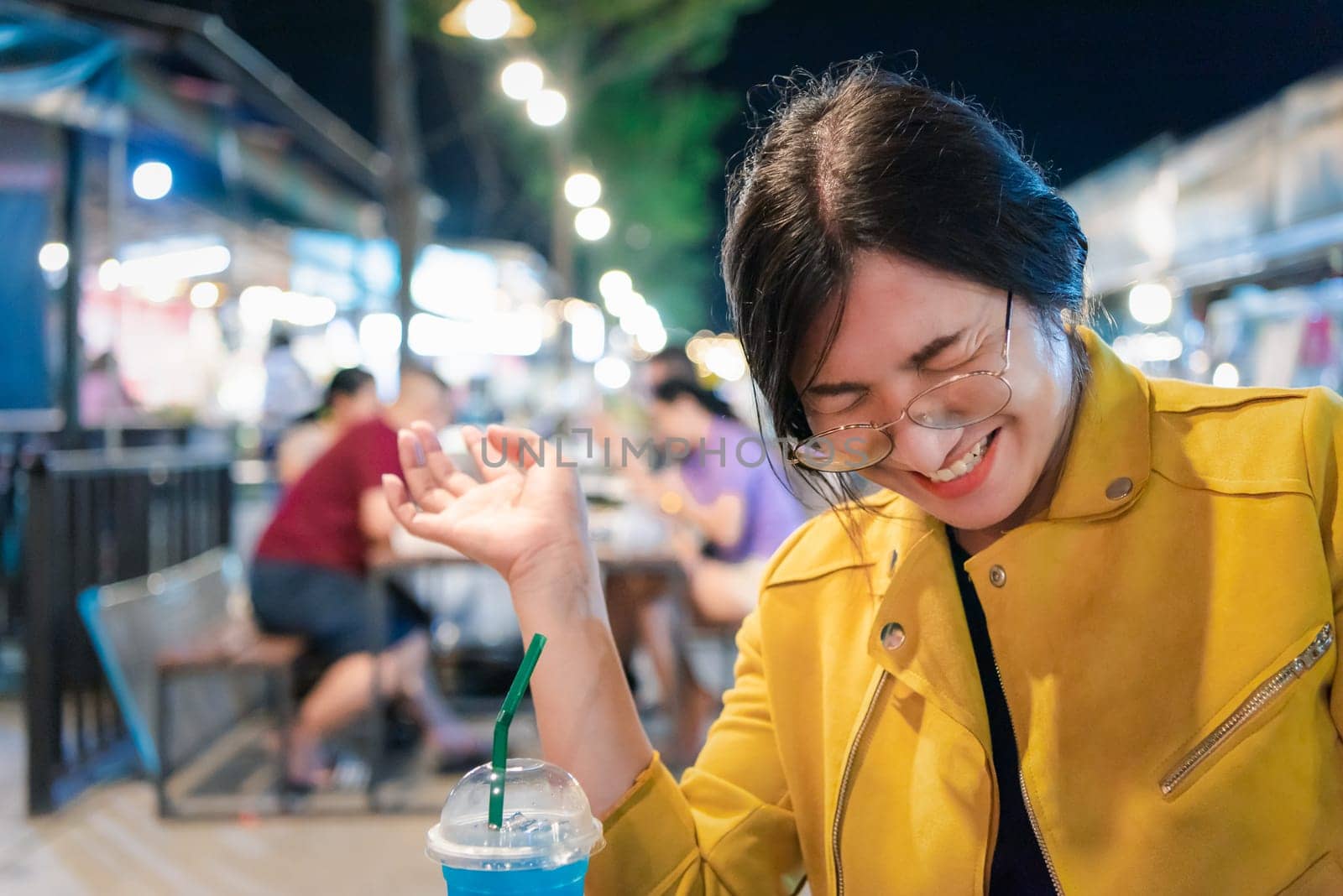 Beautiful asian woman (LGBTQ) natural makeup wear fashion yellow leather clothes with glasses posing with food or drink at thai street food, market or restaurant outdoor fashion style