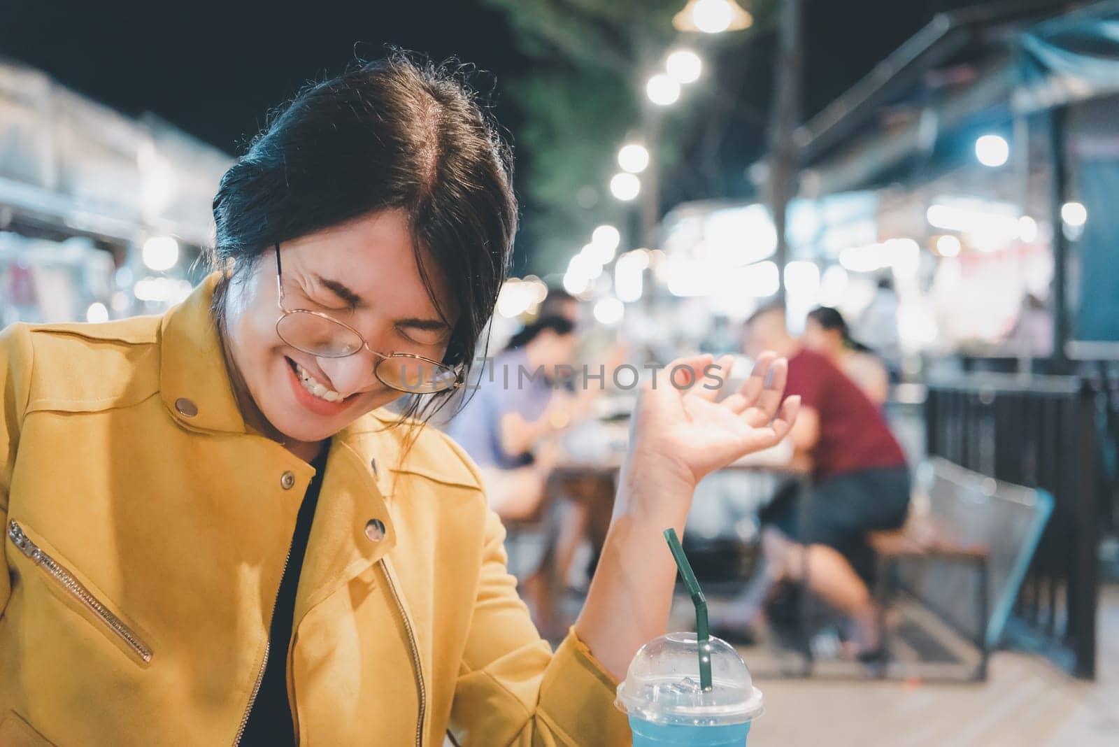 Beautiful asian woman (LGBTQ) natural makeup wear fashion yellow leather clothes with glasses posing with food or drink at thai street food, market or restaurant outdoor fashion style