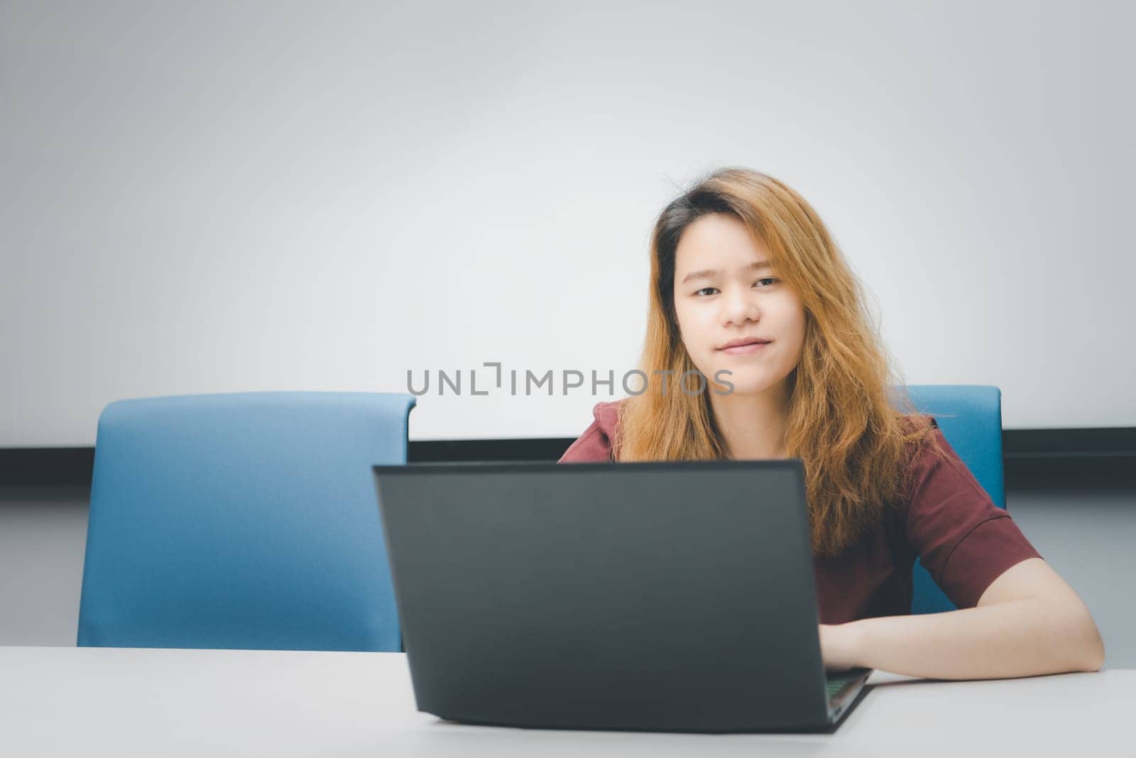 Asian woman is student, businesswoman working by computer notebook, laptop in office meeting room with whiteboard in background with happy and relax emotion in concept working woman, success in life