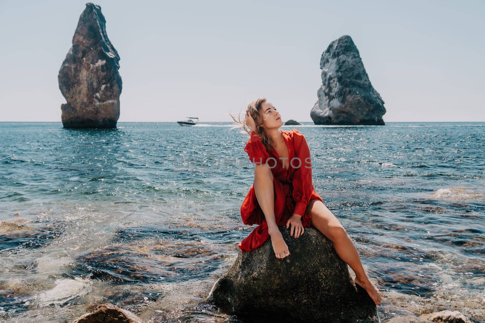 Woman summer travel sea. Happy tourist in long red dress enjoy taking picture outdoors for memories. Woman traveler posing on beach at sea surrounded by volcanic mountains, sharing travel adventure by panophotograph