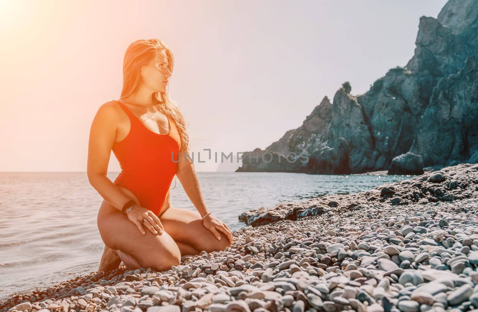 Young woman in red bikini on Beach. Girl lying on pebble beach and enjoying sun. Happy lady with long hair in bathing suit chilling and sunbathing by turquoise sea ocean on hot summer day. Close up by panophotograph