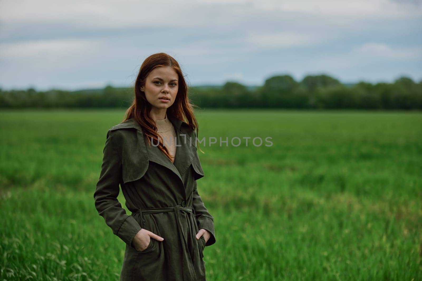 a beautiful woman stands in a green field and adjusts her coat. High quality photo