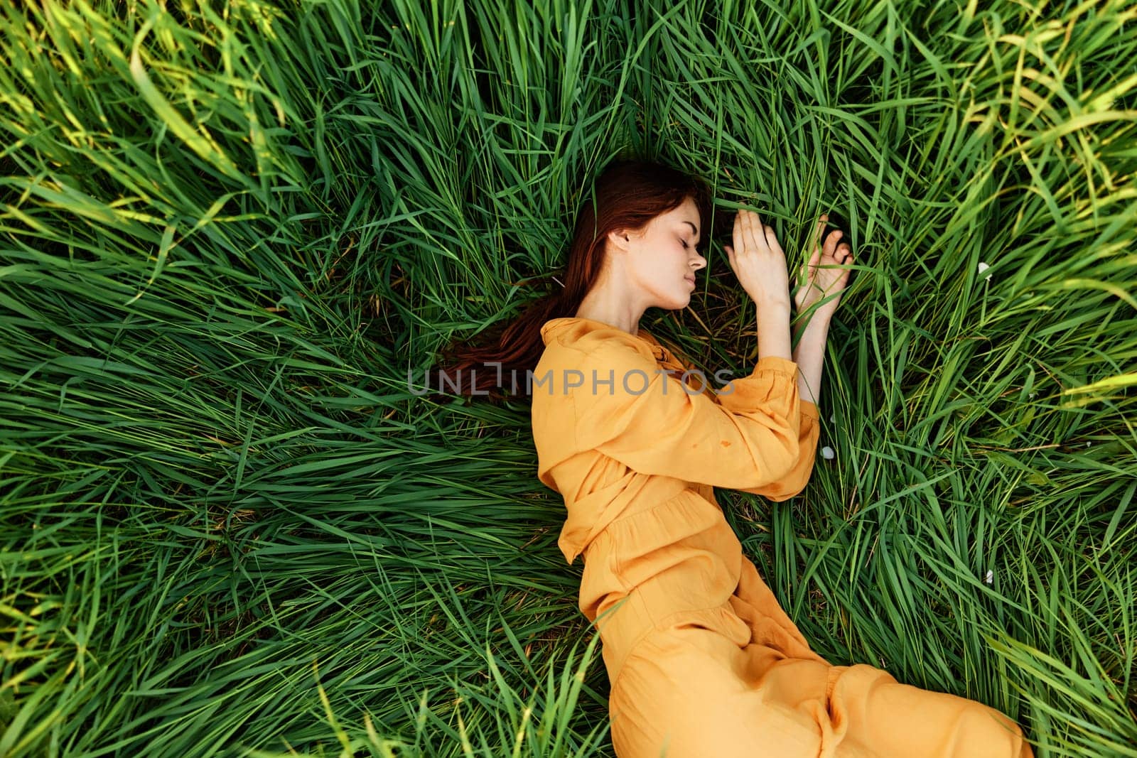 a relaxed woman enjoys summer lying in the tall green grass with her eyes closed. Photo taken from above by Vichizh