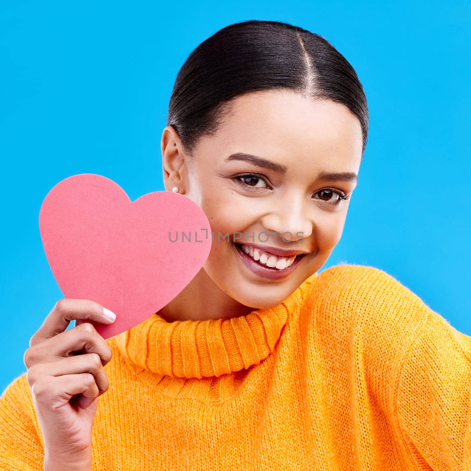 Paper heart, smile and portrait of woman in studio, blue background and backdrop. Happy female model, love shape and care of trust, support and thank you for kindness, valentines day and emoji icon by YuriArcurs