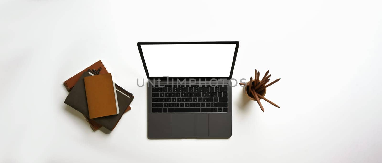 Above view of laptop computer with empty screen, books and pencil holder on white background.
