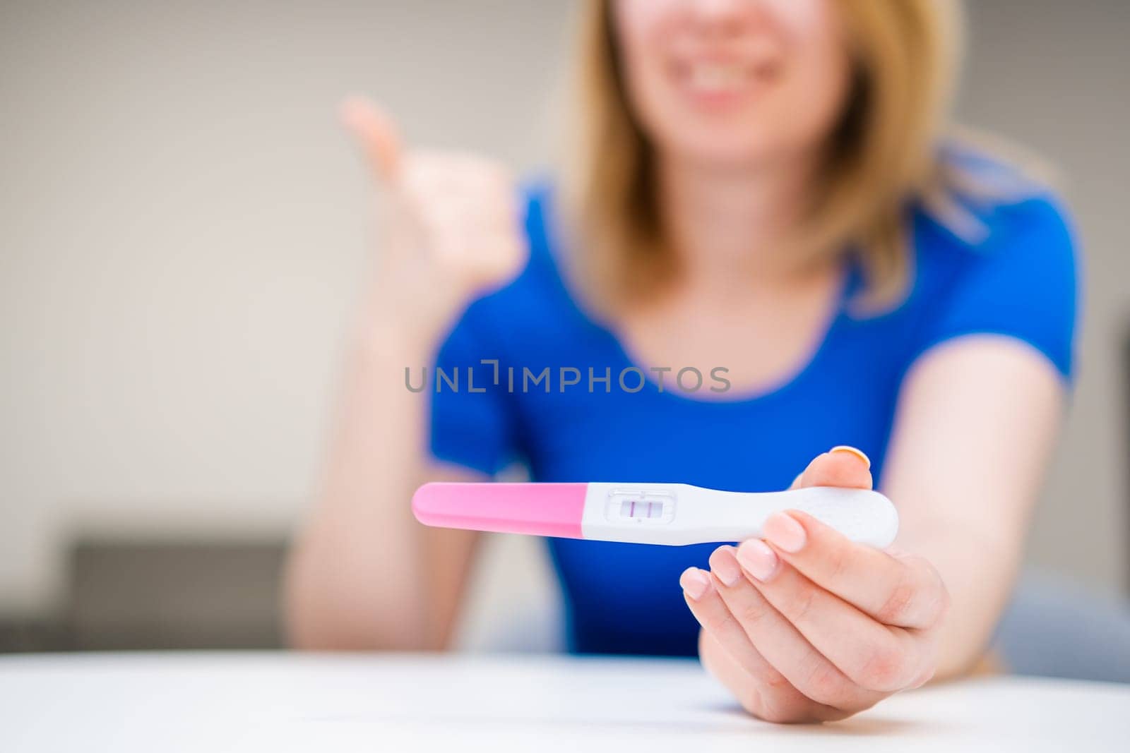 A young smiling woman shows like and holding a positive test. Expected of baby