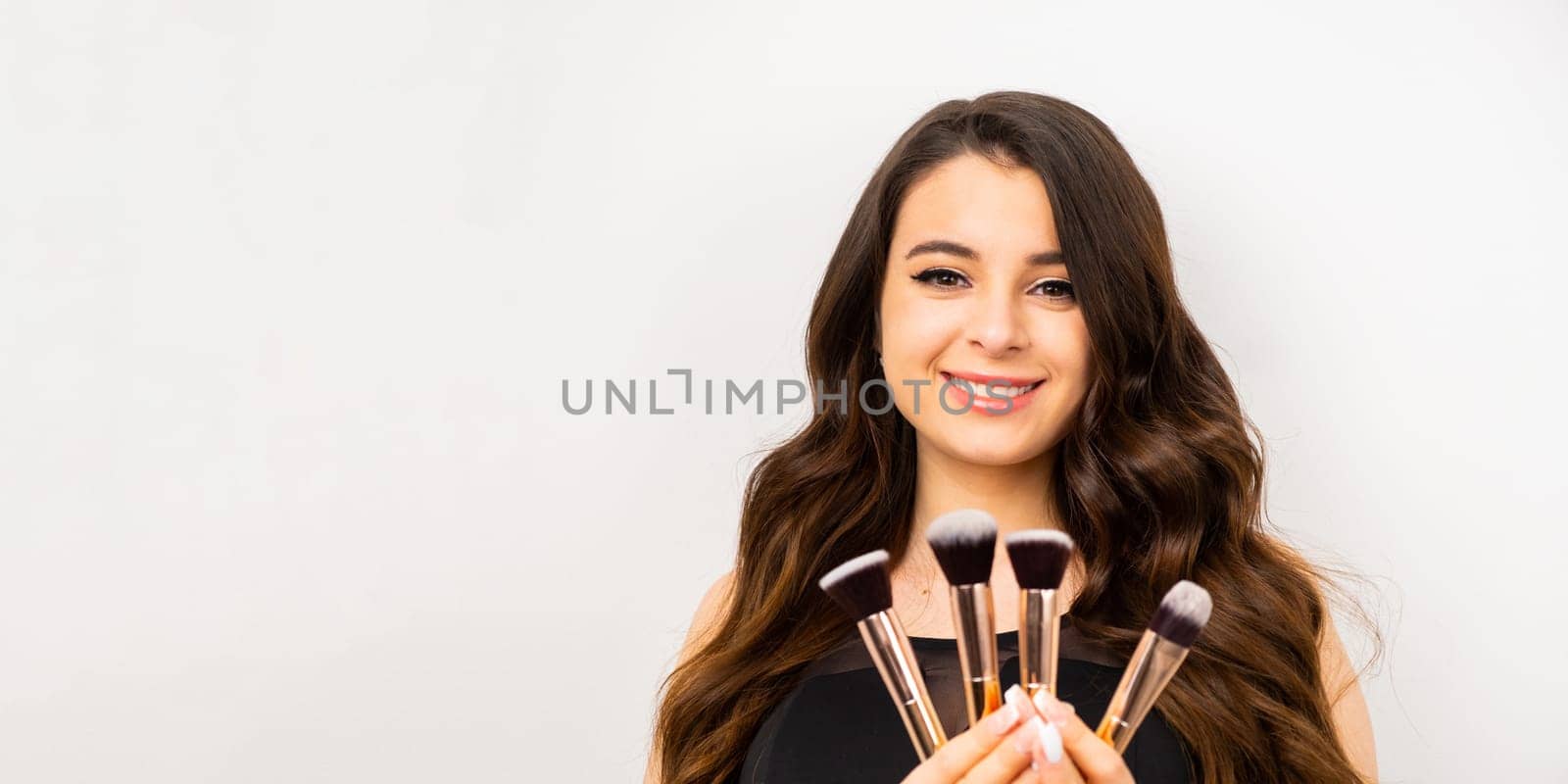 Positive attractive woman holding cosmetic makeup brushes over gray background by vladimka
