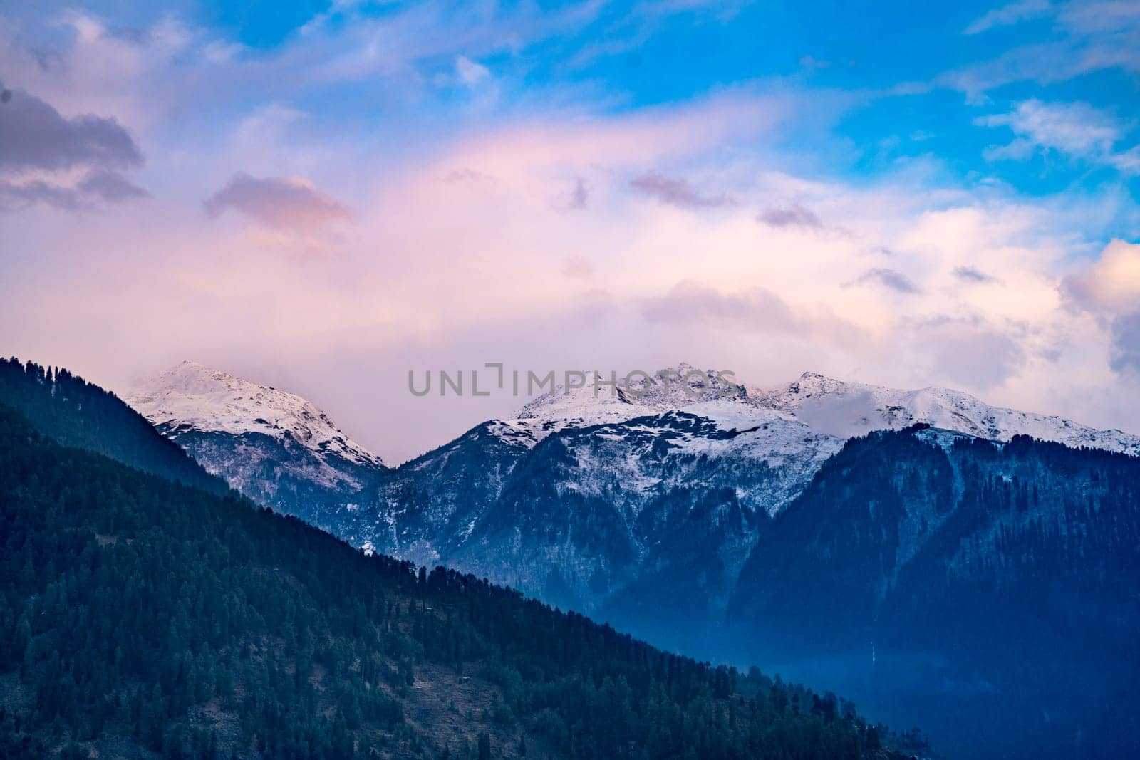 monsoon clouds moving over snow covered himalaya mountains with the blue orange sunset sunrise light over kullu manali valley by Shalinimathur
