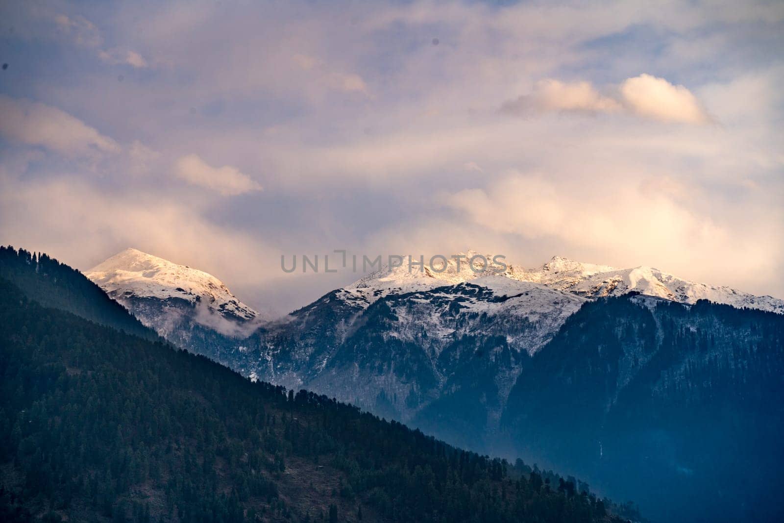 monsoon clouds moving over snow covered himalaya mountains with the blue orange sunset sunrise light over kullu manali valley by Shalinimathur