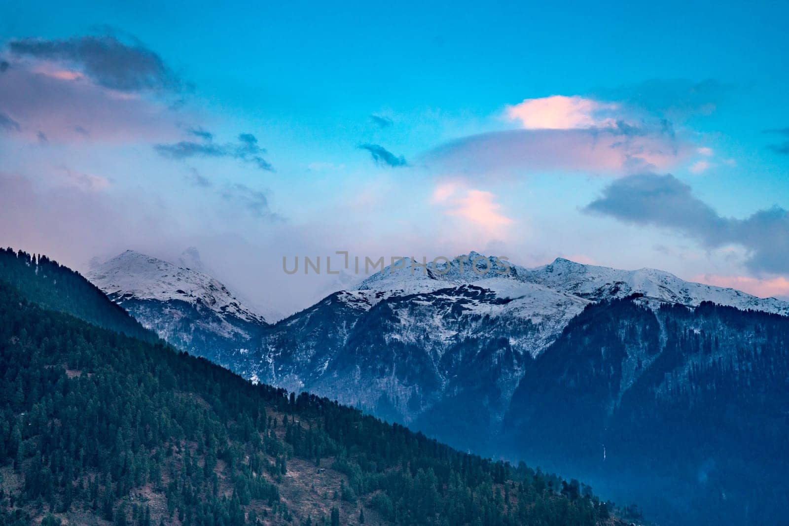 monsoon clouds moving over snow covered himalaya mountains with the blue orange sunset sunrise light over kullu manali valley India