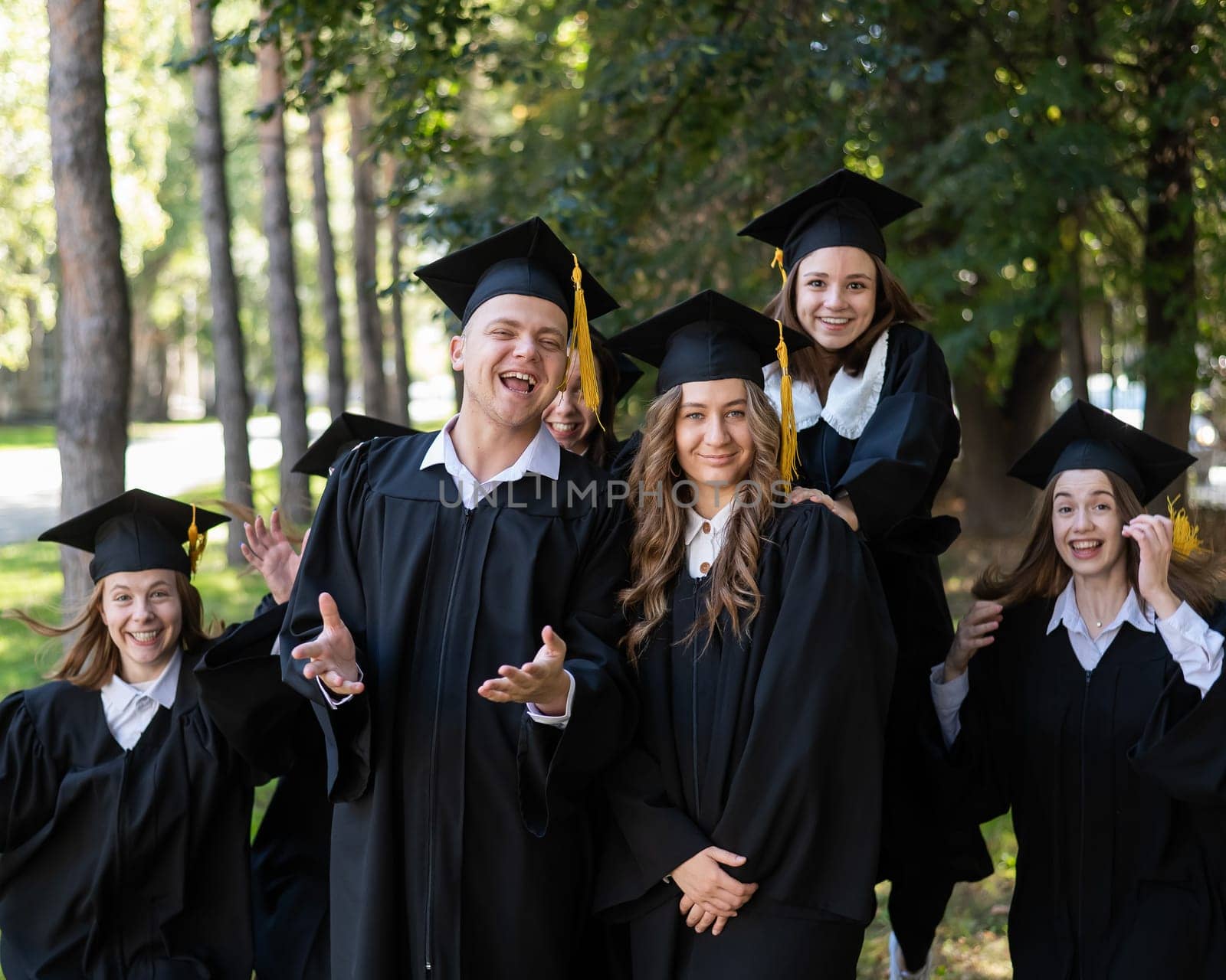 A group of graduates in robes congratulate each other on their graduation outdoors. by mrwed54