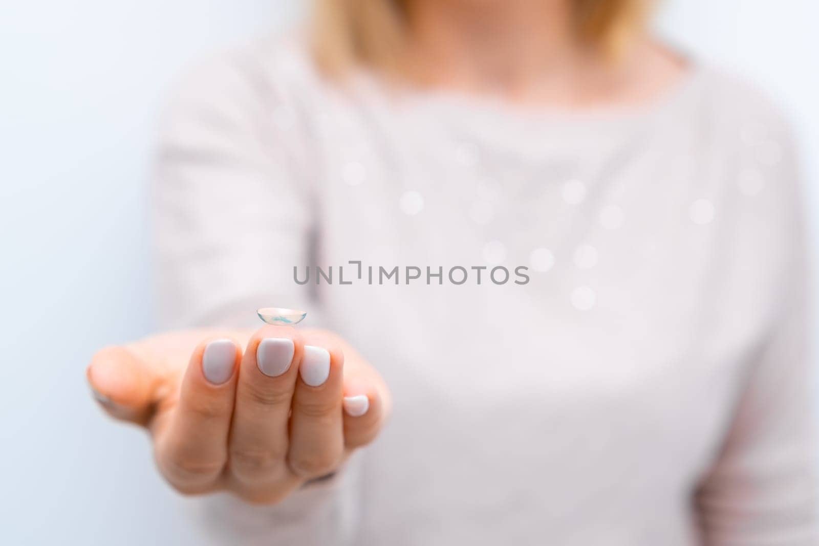 Woman in the pink sweater holding a contact lens on the tip of the contact lens. Eyes care concept