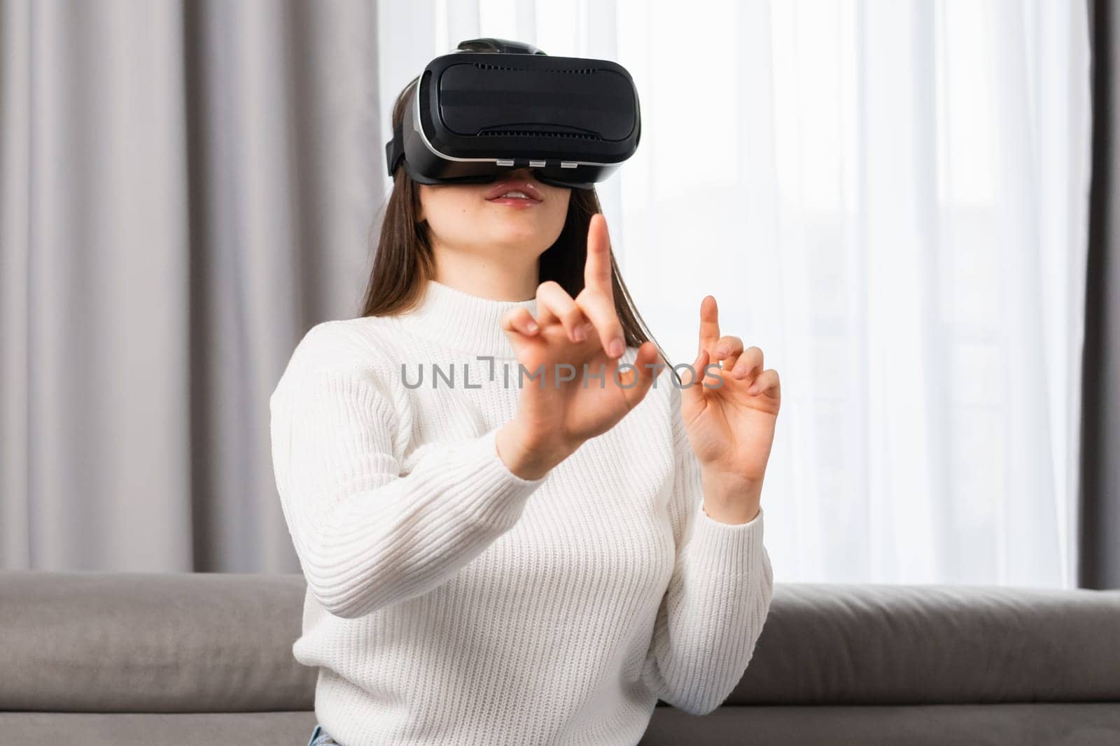 A beautiful teen girl interacts with virtual reality and touches an invisible interface sitting on the safe in the living room
