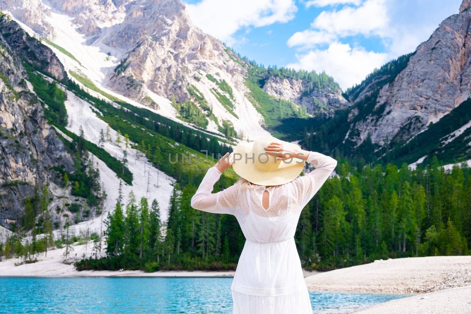Beautiful woman in a white dress walking on the shore of Lake Braies with an amazing view of the alps.