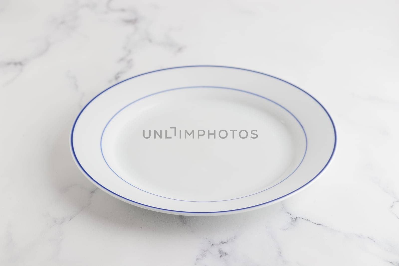 Empty white dinner plate with blue stripe on a white background