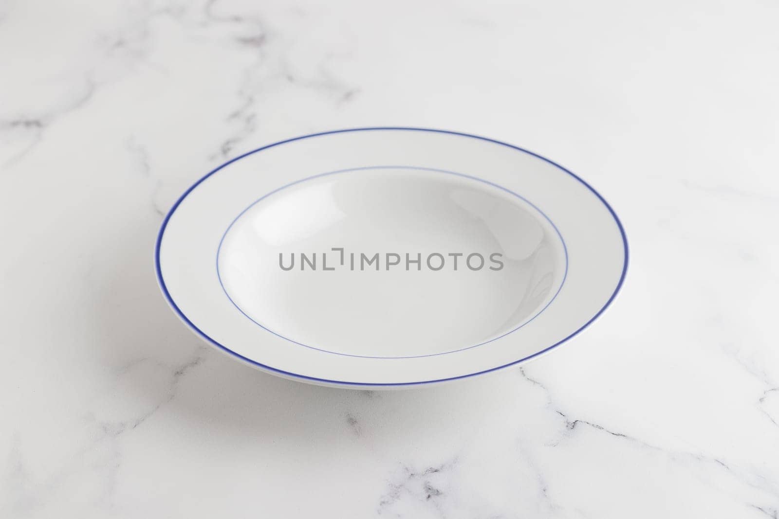 Empty white soup plate with blue stripe on a white background