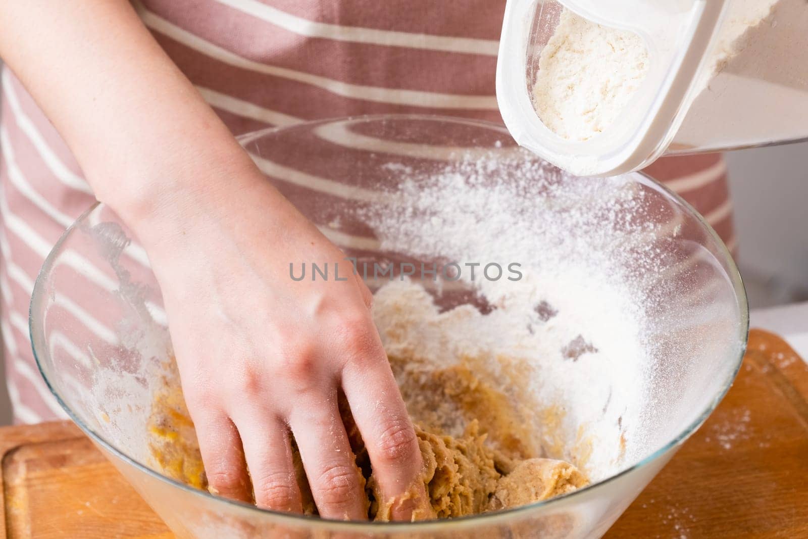 Close up of woman baker hands kneading the dough and add flour in the mixing bowl. Homemade pastry for cakes or cookies.