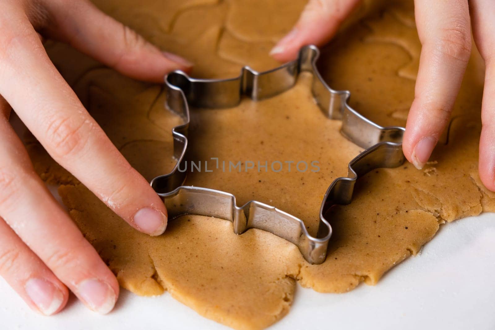 Close up woman hands cutting out cookies with metal mold from the shortcrust pastry. A metal forms in the form of snowflakes for making gingerbread for Christmas.