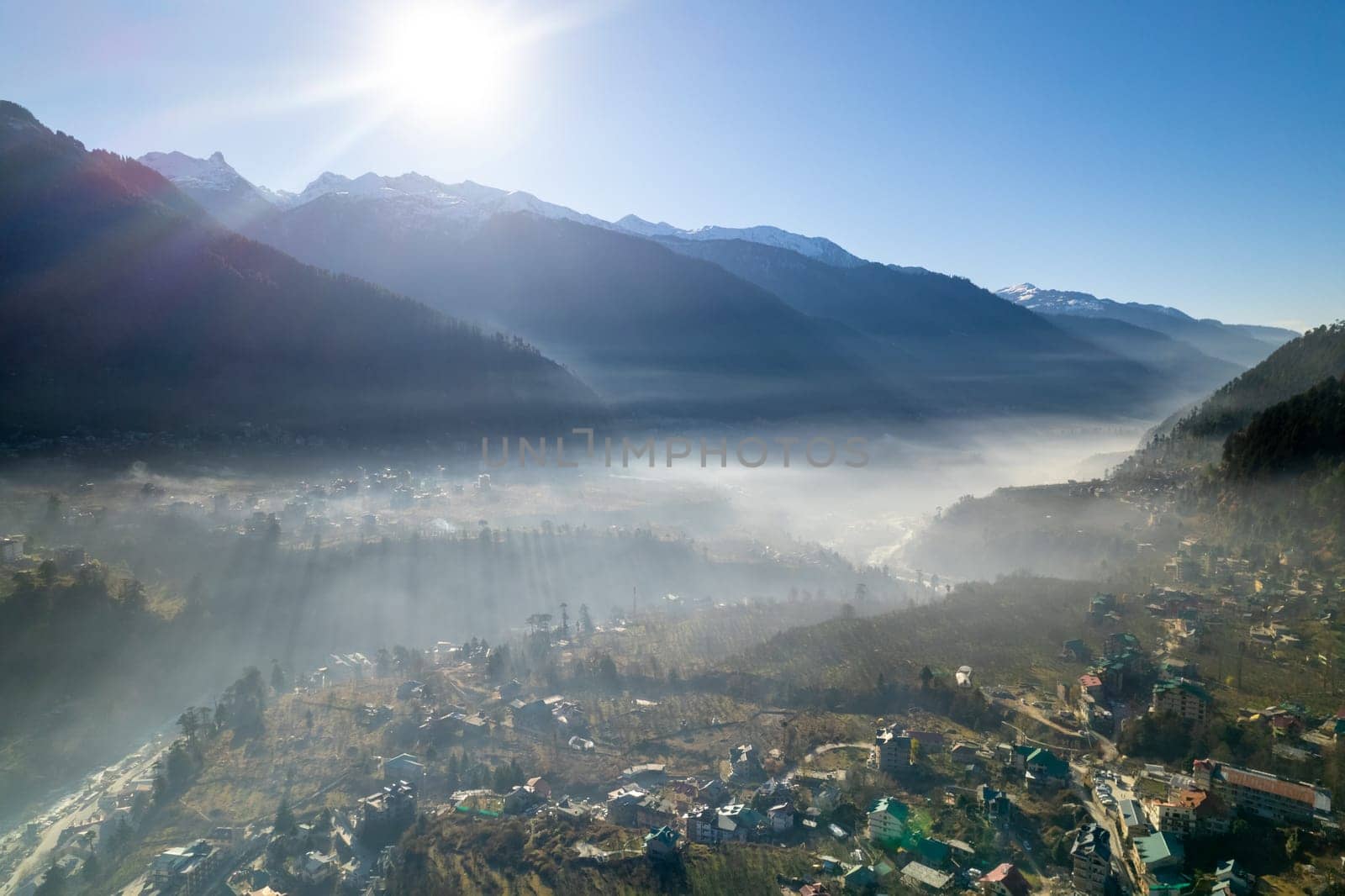 aerial drone shot gaining height over fog covered valley town of manali hill station with himalaya range in distance showing this popular tourist destination by Shalinimathur