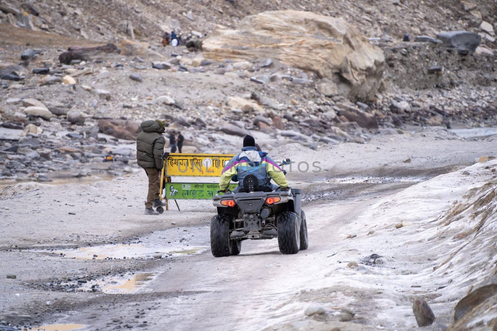 Manali, India - circa 2023: crowd of people at lahul spiti showing small food outlets, adventure sports with family riding ATV on the snow covered road with himalay peaks in the distance