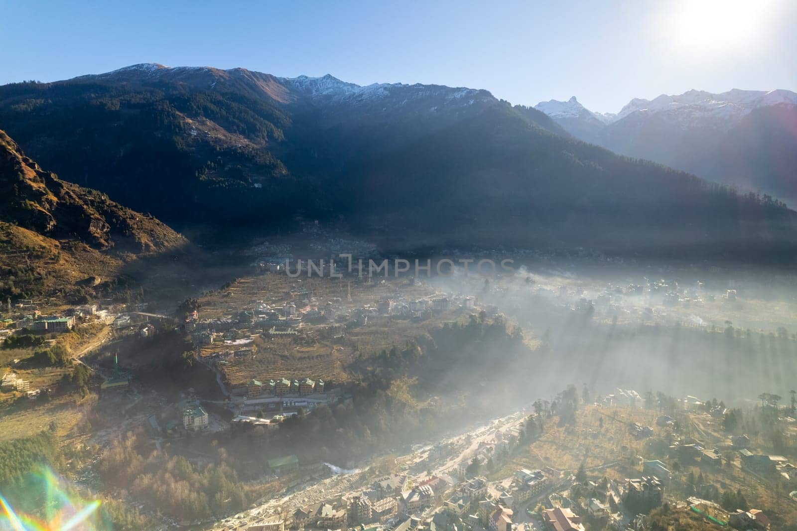 aerial drone shot gaining height over fog covered valley town of manali hill station with himalaya range in distance showing this popular tourist destination by Shalinimathur