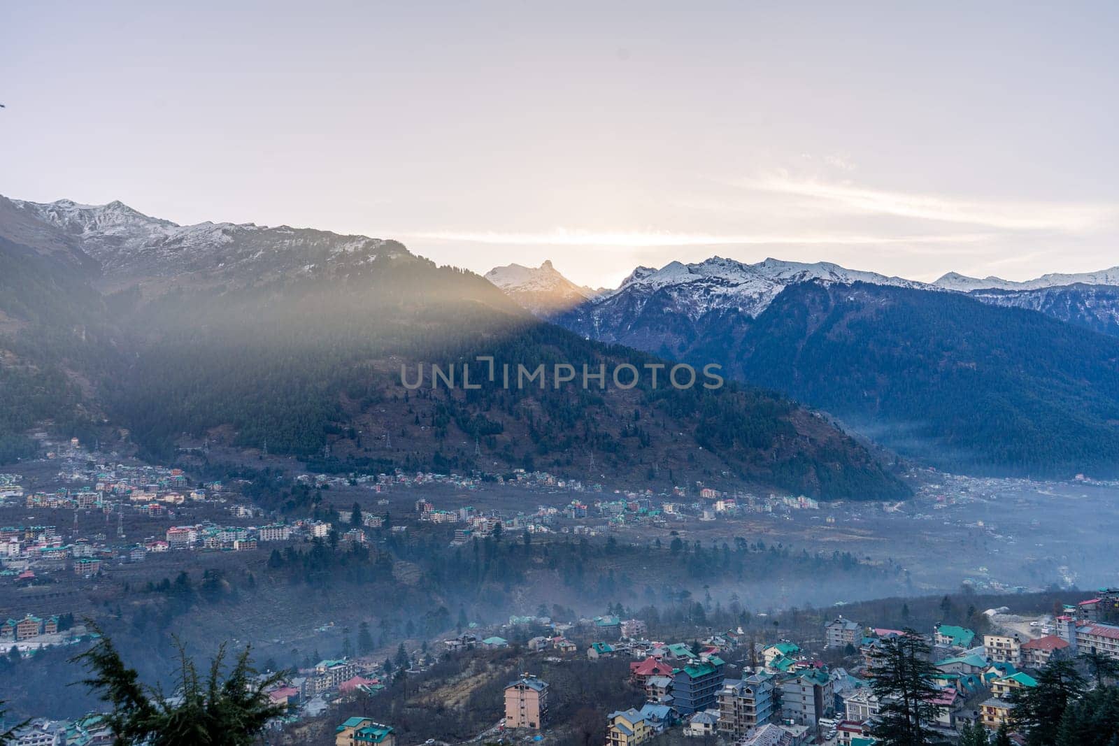 monsoon clouds moving over snow covered himalaya mountains with the blue orange sunset sunrise light with town of kullu manali valley at the base of mountains India